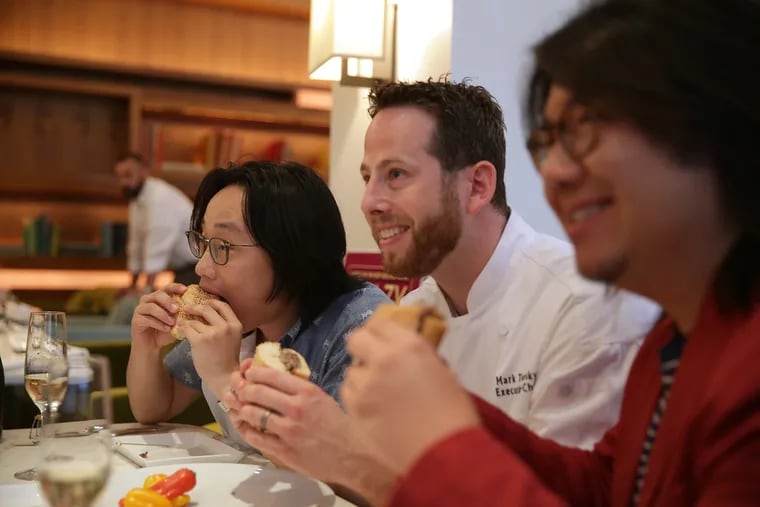 Actor Jimmy O. Yang, left, takes a bite of the $120 Philly cheesesteak as Chef Mark Twersky, center, and writer Kevin Kwan, right, pose during a promotional event for the movie "Crazy Rich Asians" at Barclay Prime in Philadelphia, PA on July 31, 2018.