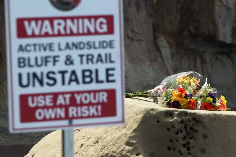 With a warning sign in the foreground, a bouquet of flowers are placed on some of the sand rock debris from Friday's bluff collapse, which killed three people, near the Grandview beach access stairway on Saturday, Aug. 3, 2019, in Encinitas, Calif.