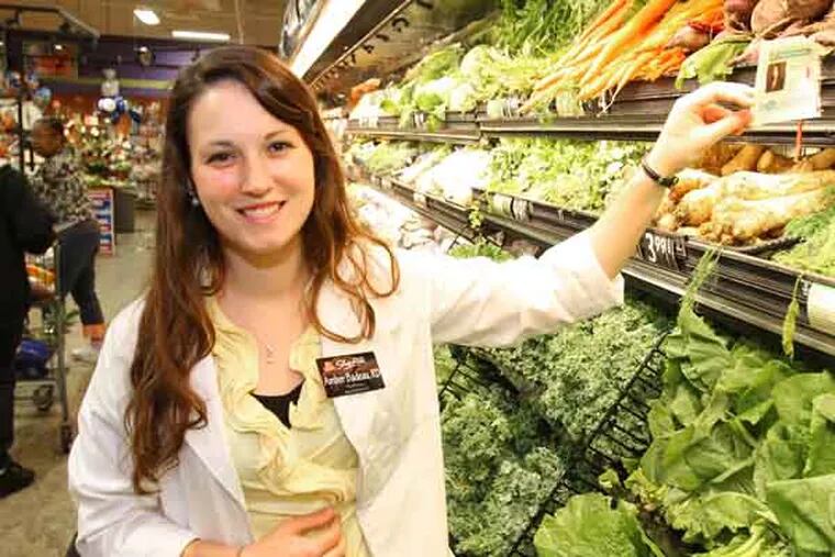 Amber Badeau, RD, right, works at a ShopRite in Olney, but she doesn't stock the shelves or ring up customers. She's a fulltime registered dietician, one of several that ShopRite has put in its stores in the mid-Atlantic region. She has a full roster of in-store programs, including free samples of healthy snacks, weight-loss challenges, and recipes using fresh seafood and vegetables. She shows the tags with her photo that highlight certain foods, such as these beets, throughout the store on July 2, 2013.    ( CHARLES FOX / Staff Photographer )