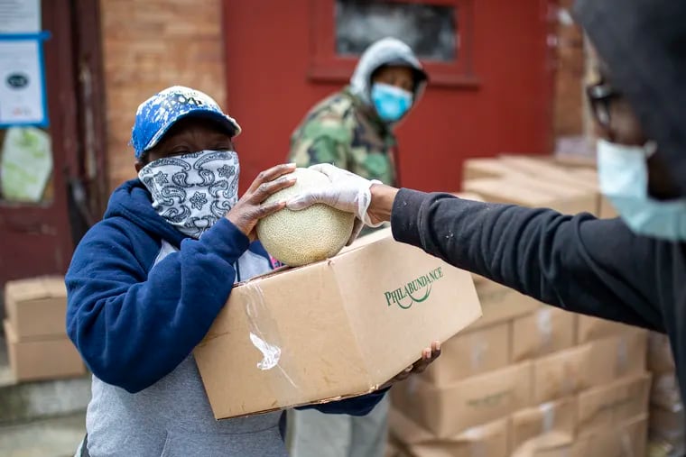 Joseph Hill, 25, of West Philadelphia, a volunteer, hands out fresh green beans or cantaloupe along with the boxes of packaged food from Philabundance to a local in the area at the corner of 59th Street and Lansdowne Avenue on Thursday, April 23, 2020. One box is provided per household and contain either nonperishable items on Mondays and fresh produce on Thursdays.
