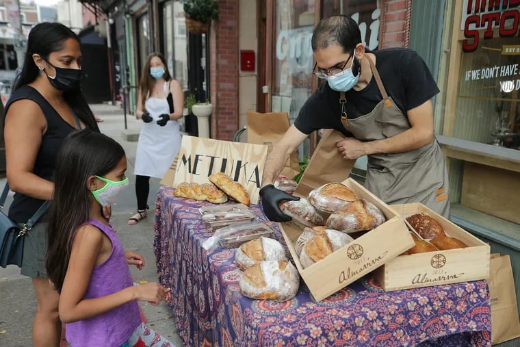 Ran Betite helps customers outside Cohen and Co. Hardware in Philadelphia on September 27. He began making bread to do something productive during the early days of the pandemic and in September launched a business named Metukah Fresh Baked. Wearing an apron, in the background, is his wife Yael Cooperman