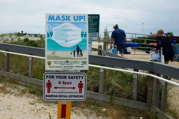 Pedestrians walk to the Strathmere, New Jersey beach past mask wearing and social distancing signs on Thursday, June 25, 2020.