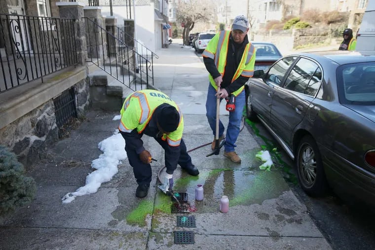 Philadelphia Water Department customer service supervisor Joe Ferretti, right, watches as utility representative Michael Cossie dye-tests stormwater and sanitary sewer connections to investigate crossover issues, in which household sewage flows into the stormwater system and vice versa, on Ainslie Street in East Falls on Friday, March 16, 2018.