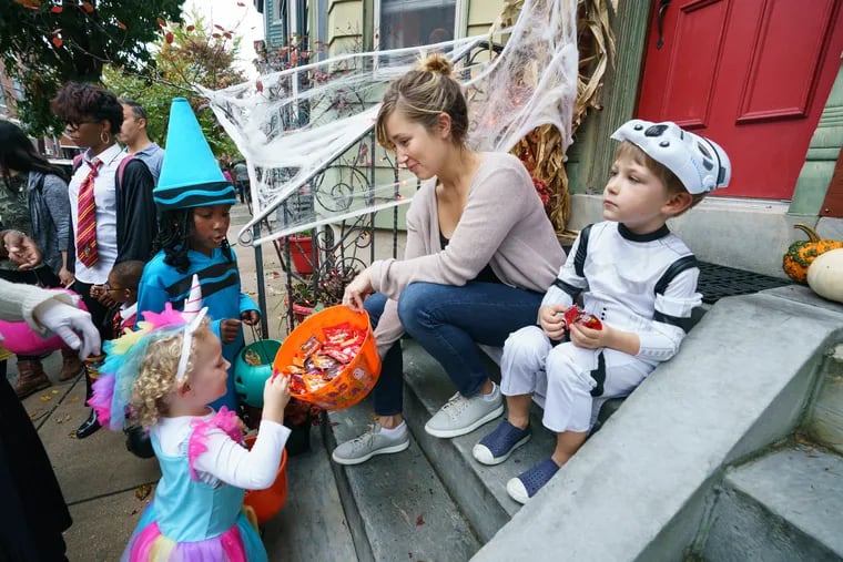 Zendaya Payne, dressed as a blue crayon, and Fiona Dunne, dressed as a unicorn, receive candy from Erin Smith and her son Sebastian while trick-or-treating in Philadelphia in 2019.