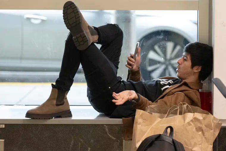 A delayed traveler uses his phone at the Philadelphia International Airport in 2022.