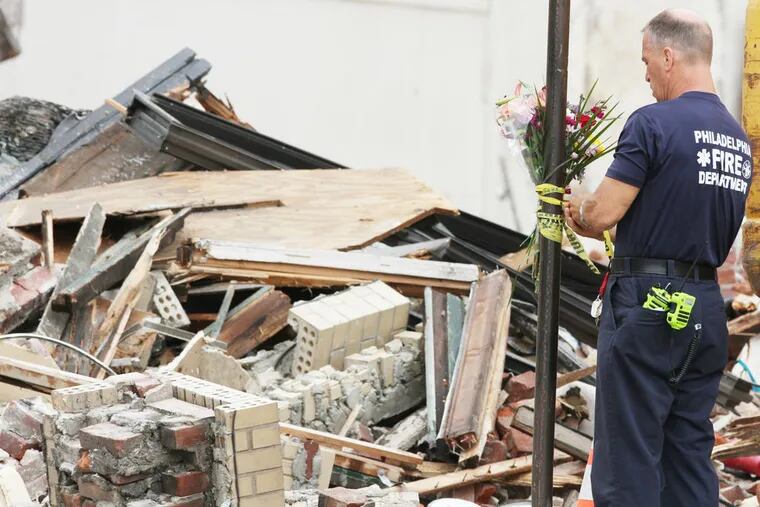 A firefighter ties several bouquets of flowers on a pole at 22nd and Market streets. They were originally on the front of the Salvation Army thrift store but were moves so the store facade could be torn down.  A adjacent building collapsed on the thrift store on June 5, killing 6 in the store.  ( CHARLES FOX / Staff Photographer )
