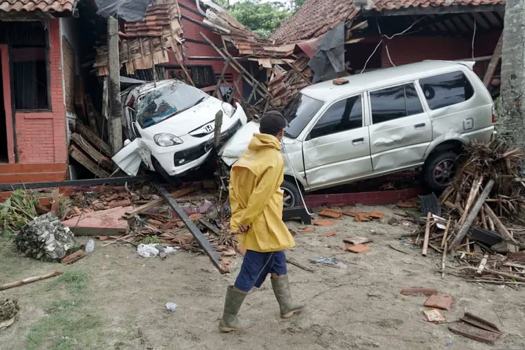 A villager walks past a car damaged by a tsunami, in Carita, Indonesia, Sunday, Dec. 23, 2018. The tsunami apparently caused by the eruption of an island volcano killed a number of people around Indonesia's Sunda Strait, sending a wall of water crashing some 65 feet (20 meters) inland and sweeping away hundreds of houses including hotels, the government and witnesses said. (AP Photo/Dian Triyuli Handoko)