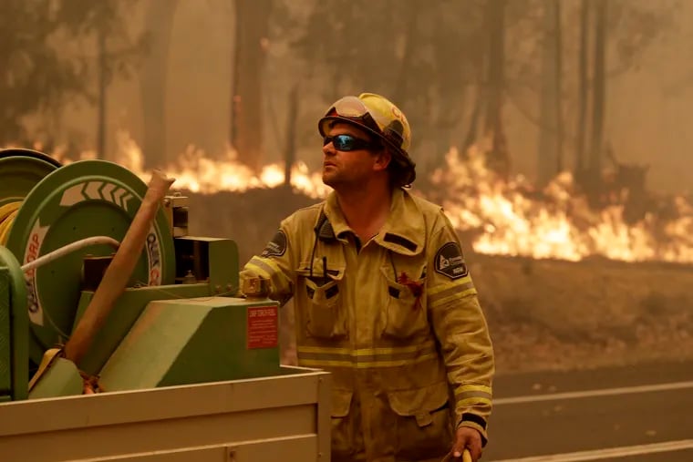 A Forest Corporation worker manages a fire hose as he battles a fire near Moruya, Australia, Saturday, Jan. 4, 2020. Australia's Prime Minister Scott Morrison called up about 3,000 reservists as the threat of wildfires escalated Saturday in at least three states with two more deaths, and strong winds and high temperatures were forecast to bring flames to populated areas including the suburbs of Sydney.