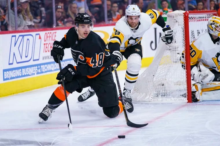 Philadelphia Flyers' Morgan Frost, left, handles the puck as Pittsburgh Penguins' Brian Dumoulin, right, comes after him during the second period of an NHL hockey game, Sunday, April 24, 2022, in Philadelphia. (AP Photo/Chris Szagola)
