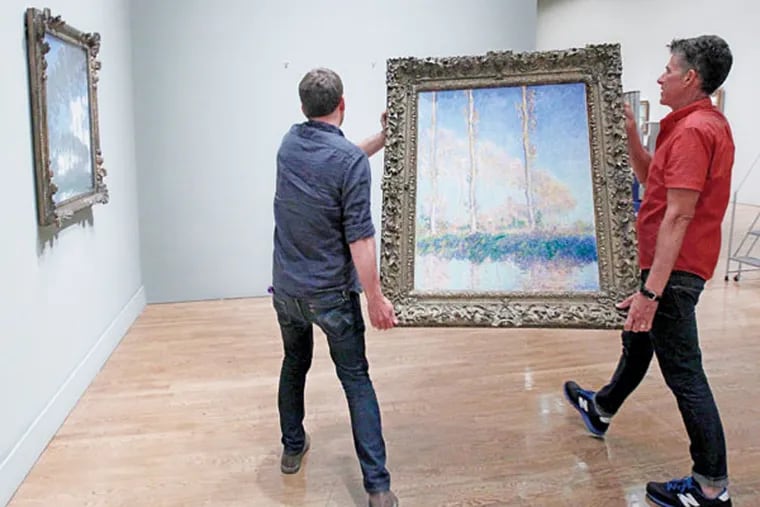 Gus Boyce (left) and Eri Griffin, installers at the Philadelphia Museum of Art, hang Monet’s “Poplars
on the Banks of the River Epte” for the exhibit. (MICHAEL BRYANT/Staff Photographer)