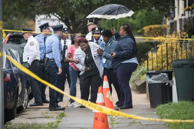 A grieving woman is assisted outside a home where four people were found shot dead Wednesday, Oct. 30, 2019, in west Philadelphia. Police say a man is in custody following the deaths of his mother, stepfather and two brothers, including a 6-year-old boy, who were found shot in the home. (Charles Fox/The Philadelphia Inquirer via AP)