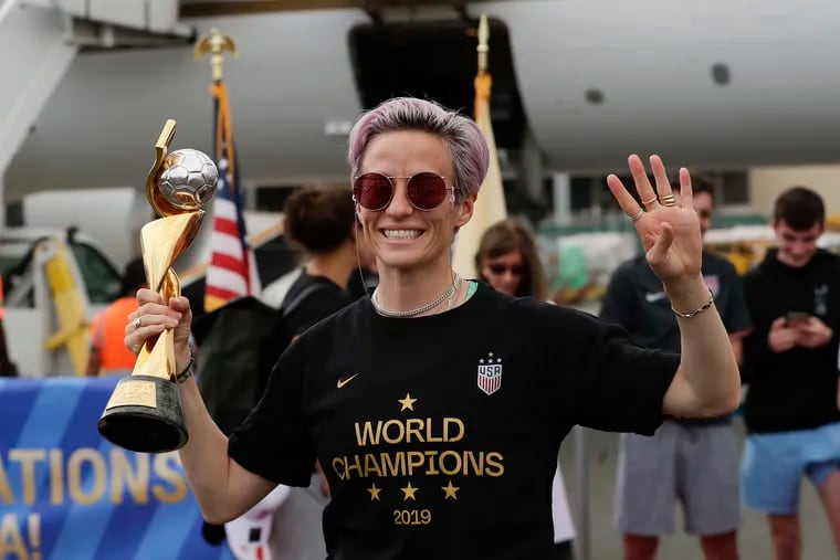 U.S. Women's World Cup champions team member Megan Rapinoe holds the trophy and raises four fingers for the team's fourth Women's World Cup championship, after arriving at Newark Liberty International Airport in Newark on Monday.