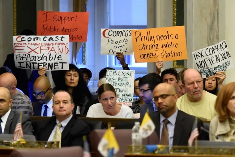 Spectators hold signs during a City Council hearing on the proposed franchise agreement with Comcast on Nov. 12, 2015.