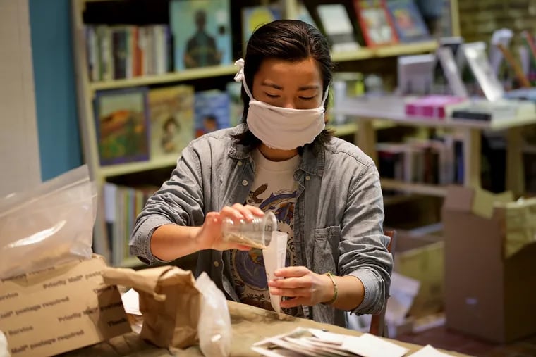 Volunteer Shelby Kim fills an envelope with cherry tomato seeds inside the Making Worlds bookstore, which opened in February and had to close during the pandemic. The ownership collective agreed to share the space for a massive seed distribution effort.