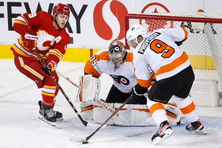Flyers degfenseman Ivan Provorov battles for the puck with the Calgary Flames' Matthew Tkachuk in front of Flyers goalie Carter Hart during the second period on Saturday, Oct. 30, 2021, in Calgary, Alberta.