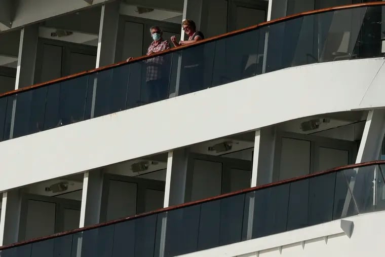 Passengers, one wearing a protective face mask, look out from the Zaandam cruise ship.