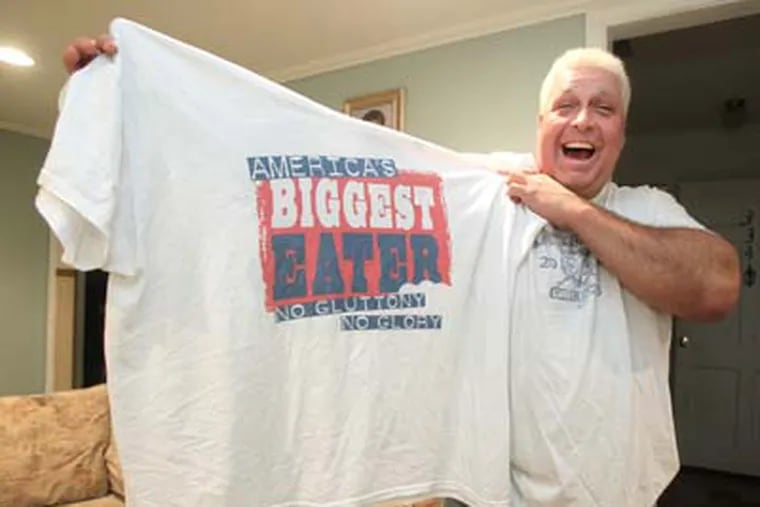 El Wingador, who in real life is retired 50-year-old truck driver Bill Simmons (CQ - HE WAS ALSO CALLED BOB ON THE PHOTO ASSIGNMENT BUT IT IS BILL) from Woodbury Heights, has now retired also from competitive eating, after being a five-time WIng Bowl champ. He is trying to sell a reality show, "America's Biggest Eater",  in which he would be an adviser to gluttonous competitive eaters.  He holds up a 4XL T-shirt that is even too big for him.   ( Charles Fox / Staff Photographer )  JWING23P, 2/16/2012, BILL SIMMONS (CQ), 334 IVY DRIVE, WOODBURY HEIGHTS, NJ