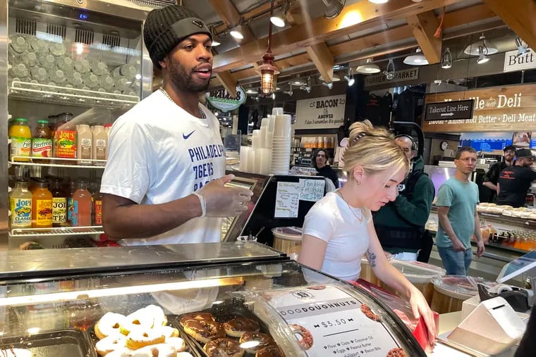 Buddy Hield, acquired by the Sixers in a trade with the Pacers and Spurs last month, works behind the counter with Maddi Tunney (right) at Beiler’s Doughnuts in Reading Terminal Market Friday, Mar. 15, 2024.