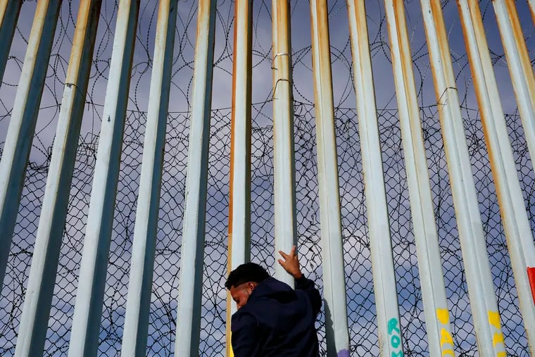 A man holds on to the border wall along the beach, Tuesday, Jan. 8, 2019, in Tijuana, Mexico.