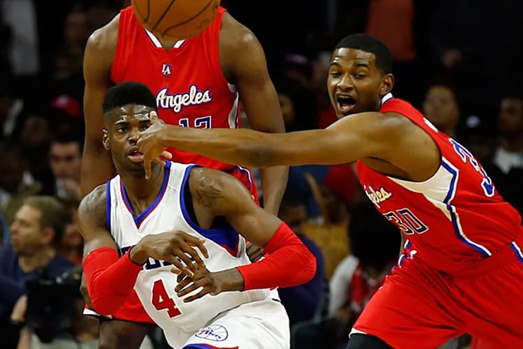 Sixers' Nerlens Noel passes the basketball from his knees past Clippers' C.J. Wilcox.  (YONG KIM/Staff Photographer)