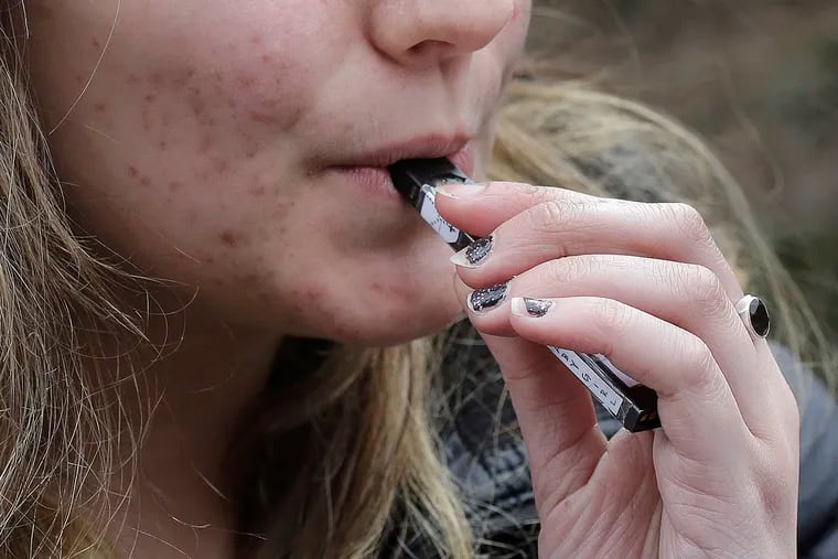 FILE - In this April 11, 2018 file photo, a high school student uses a vaping device near a school campus in Cambridge, Mass. A new study released Wednesday, Sept. 18, 2019, found another jump in how many U.S. teens vape nicotine-tinged electronic cigarettes. About 25% of high school seniors surveyed this year said they vaped nicotine in the previous month, up from about 21% the year before  .(AP Photo/Steven Senne, File)