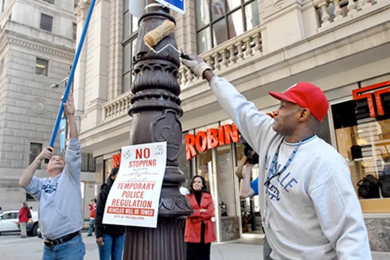 Philadelphia police officer Richard Whitford, left, and custodial worker Rufus Belton apply lubricant to a utility pole near Broad and Chestnut Streets to prevent any celebratory climbs by Phillies fans should the team win the pennant tonight. (April Saul / Staff Photographer)