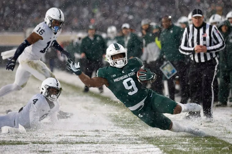 Michigan State's Kenneth Walker III, right, slips out of bounds on a run against Penn State's Kalen King (4) and Ji'Ayir Brown (16) during the second quarter of an NCAA college football game, Saturday, Nov. 27, 2021, in East Lansing, Mich. (AP Photo/Al Goldis)