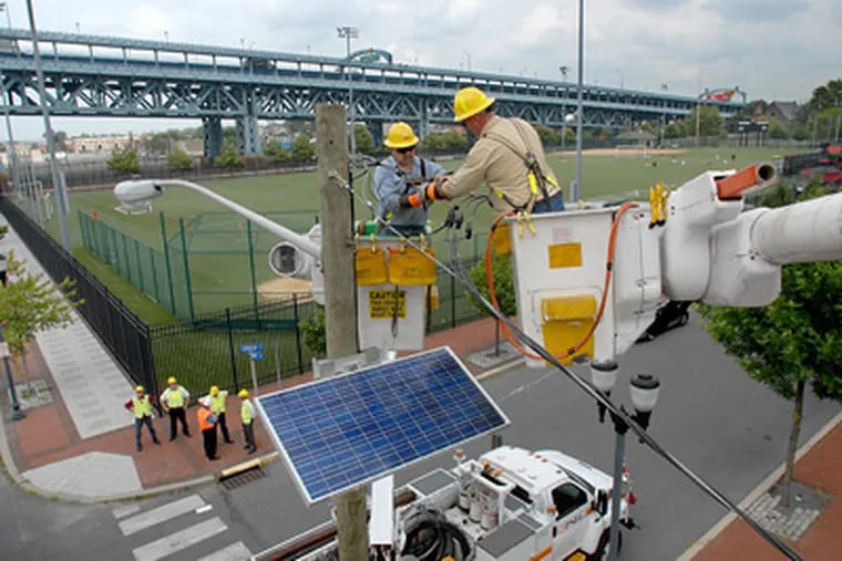 Linemen Terry Lane (left) and Mike Gregory install a solar panel at Linden Street and Delaware Avenue in Camden as part of Public Service Electric and Gas’s “Solar 4 All” project. (April Saul / Staff Photographer)