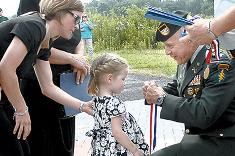 At a service for Marine First Lt. Jason Mann, daughter Isabella gets a medal from Col. John Rawley in front of Mann’s wife, Shannon, and mother, Alfina. (April Saul / Inquirer)