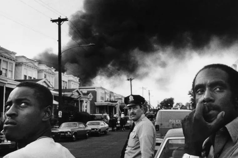 Smoke pours out over Osage Avenue after police dropped a bomb from a helicopter onto the roof of the MOVE house in West Philadelphia — and firefighters were ordered to let the fire burn. Six adults and five children died in the confrontation that day, May 13, 1985, and 61 surrounding homes were destroyed.