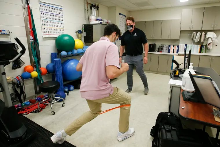 Lower Merion High School trainer Jason Luty (right) watches senior basketball player Zack Wong use an exercise band in the school's training room on June 4, 2021. Wong, who is graduating, was a forward on the basketball team.