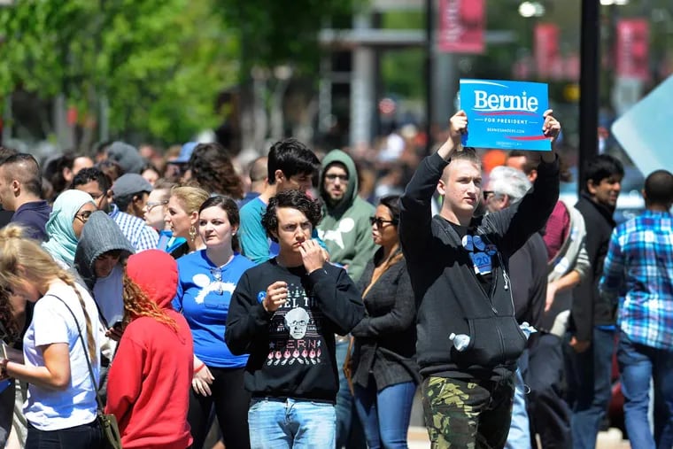 High School senior Collin Nadolsky, Somerset, NJ, holds a sign up to passing cars as he and thousands of others wait to get into Rutgers University's Louis Brown Athletic Center three hours before candidate Bernie Sanders will address the crowd May 8, 2016.