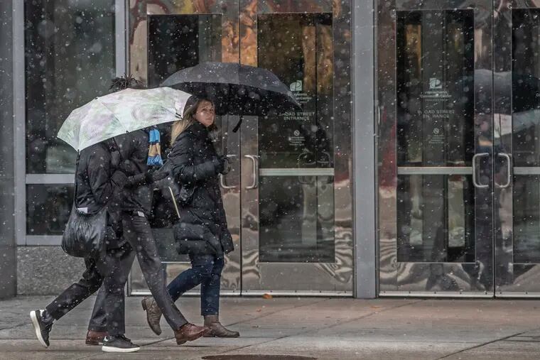 Pedestrians walking down Broad Street in front of the convention center use umbrellas to keep dry while snow falls in Center City around noon on Tuesday November 12, 2019.