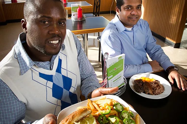 Sheldon Crosbie (left) and Zahid Khan take a novel approach to Caribbean food at the Upper Darby restaurant Bad Habit Caribbean. Crosbie is holding the Bad Habit Burger and Khan sits with a Jerk Chicken Platter. ( ALEJANDRO A. ALVAREZ / STAFF PHOTOGRAPHER )