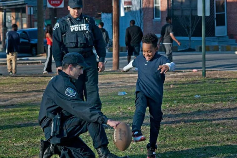 Camden County police officers Oliver Isshak (foreground) and Nicholas Voorhees played football with kids yesterday, April 1, 2014, in Camden's Whitman Park.