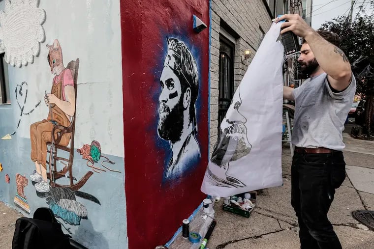 Local artist Nero, working on his Bryce Harper mural at 12th and Christian Street on Wednesday. The mural at left is not his.