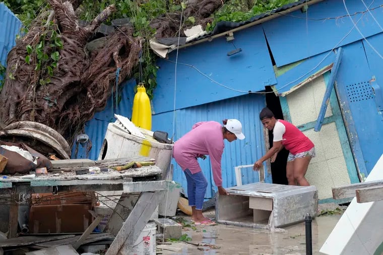 Yesenia Martinez (left) and Dilcia Figaro pick up items scattered by Hurricane Fiona in the low-income neighborhood of Kosovo in Veron de Punta Cana, Dominican Republic.