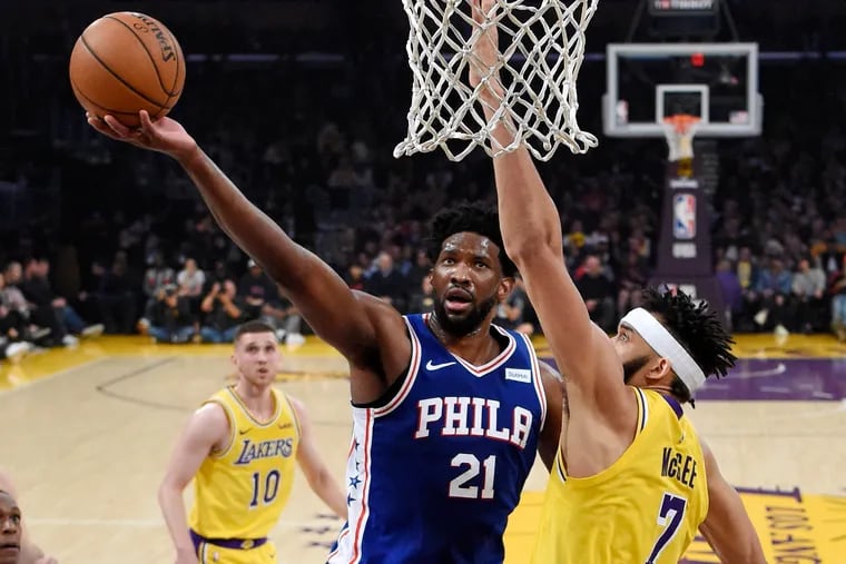 Philadelphia 76ers center Joel Embiid, center, shoots as Los Angeles Lakers center JaVale McGee, right, defends during the first half of an NBA basketball game Tuesday, Jan. 29, 2019, in Los Angeles.