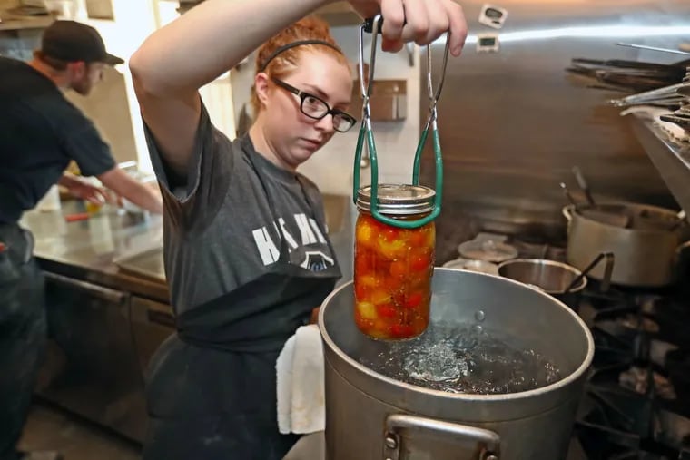 In the kitchen at the Hungry Pigeon in Queen Village, Taylor Koch lowers a sealed canning jar of locally grown tomatoes into boiling water to force the air out and create a vacuum.