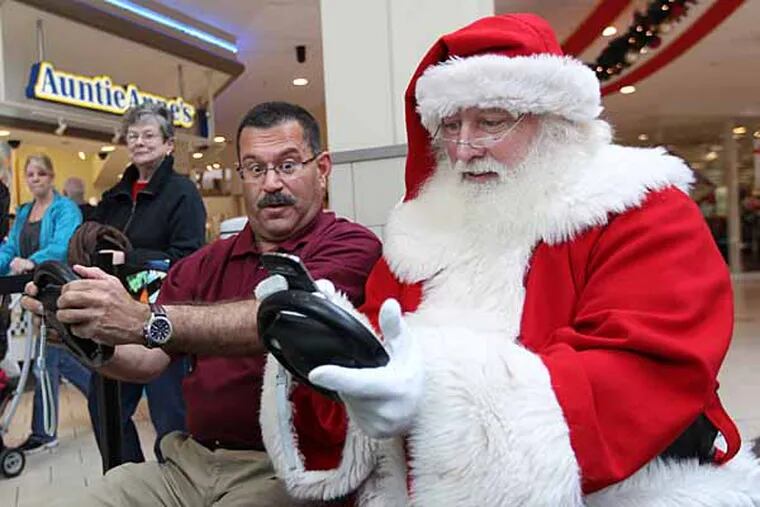 The Santa at the Voorhees Town Center , right, and Ray Martinez, the Chairman of New Jersey Motor Vehicles, center, have an audience as they drive on a simulator to show what can happen when you try to use your phone, or text while driving.  DMV comes to Voorhees Mall with an interactive booth to urge drivers to slow down and put the phone down while driving around town this holiday season. Drivers will get the chance to tackle a video driving game and wear vision-impaired glasses to find out how dangerous driving while impaired can be.  To learn the dangers of driving while distracted, DMV will invite shoppers to tackle a video driving game and don vision impaired goggles while typing a message 12/20/2012 JDRIVE21( MICHAEL BRYANT / Staff Photographer  )