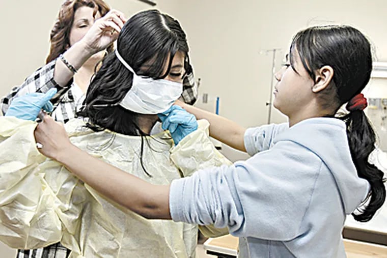 Dalia Perez, 14 (center ) gets help in putting on a gown and a mask from student service coordinator & RN, Deborah Molone and fellow student, Justine LaBoy,13 during visit to Helene Fuld School of Nursing building. (Akira Suwa / Inquirer )