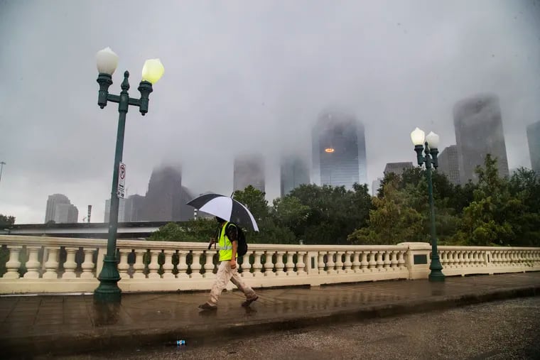A pedestrian walks on the Sabine Street Bridge on the foreground of the Houston skyline during the Tropical Storm Beta in 2020.