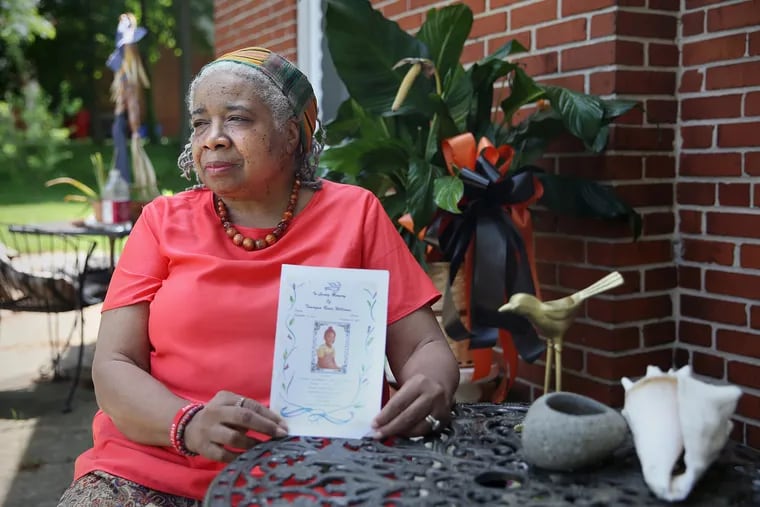 Rev. Jean Waites-Howard sits for a portrait with a program from a funeral she officiated outside her home in Norristown. Waites-Howard has delivered a number of eulogies for the West Philadelphia community where she grew up.