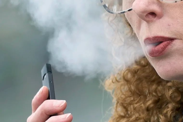 A woman exhales while vaping from a Juul pen e-cigarette in Vancouver, Wash., April 16, 2019.