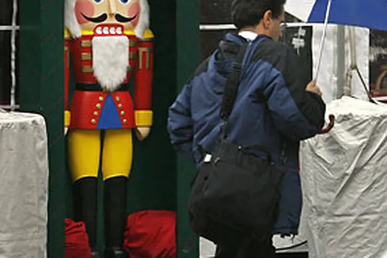 The Nutcracker in front of the Kathe Wohlfahrt shop, a vendor in the Christmas Village at Dilworth Plaza, next to City Hal,l takes shelter from the rain this morning as commuters walk past with umbrellas open.