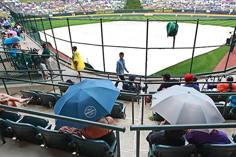 Fans hide under umbrellas after a tarp is placed over the infield at Howard J. Lamade Stadium in Williamsport, Pa. on Wednesday afternoon. (Michael Bryant/Staff Photographer)