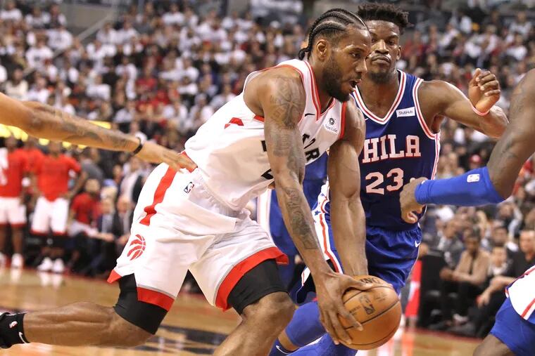 Kawhi Leonard, left, of the Raptors  drives by Jimmy bUtler, center, and other sixer defenders during the 1st half of their NBA playoff game at the Scotiabank Arena in Toronto on April 27, 2019.