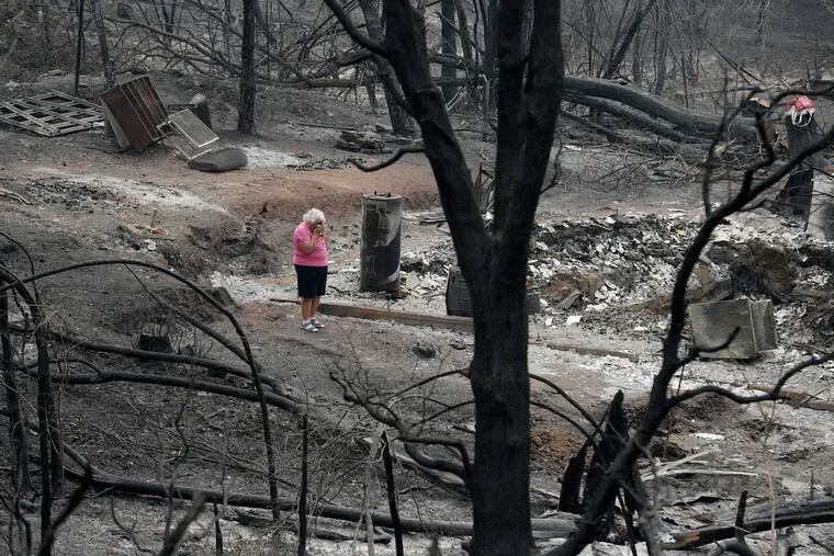 FILE – In this Aug. 9, 2018, file photo, Loretta Root wipes her eyes while visiting the remains of her home in the Keswick area burned in the Carr Fire in Redding, Calif. While California officials quickly determined an arsonist started the wildfire burning southeast of Los Angeles and that sparks from a vehicle produced the deadly wildfire in the city of Redding, causes for many of the state's worst blazes in the past decade remain a mystery. (AP Photo/John Locher, File)