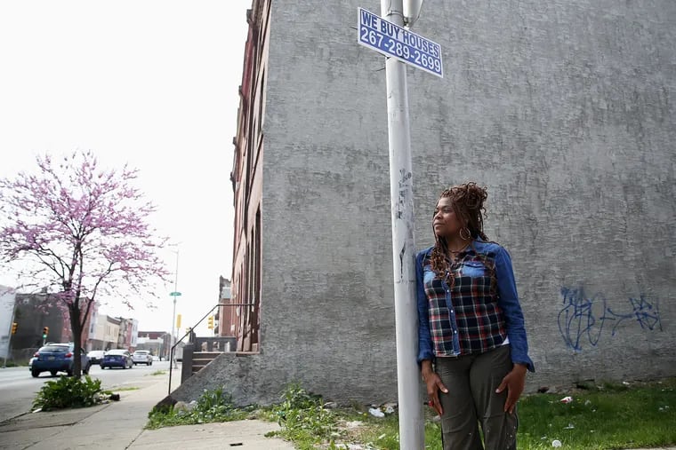 Tonetta Graham, president of the Strawberry Mansion Community Development Corporation, under a "We Buy Houses" sign in Philadelphia's Strawberry Mansion neighborhood in 2019. Her organization has urged local homeowners to be wary of unsolicited calls and pressure tactics from would-be buyers.