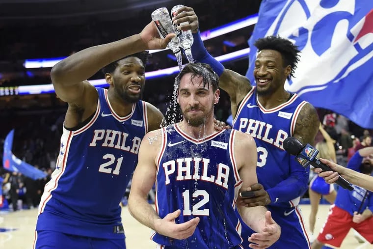 T.J. McConnell getting doused with water by teammates Robert Covington (right) and Joel Embiid at the end of Monday night’s game.